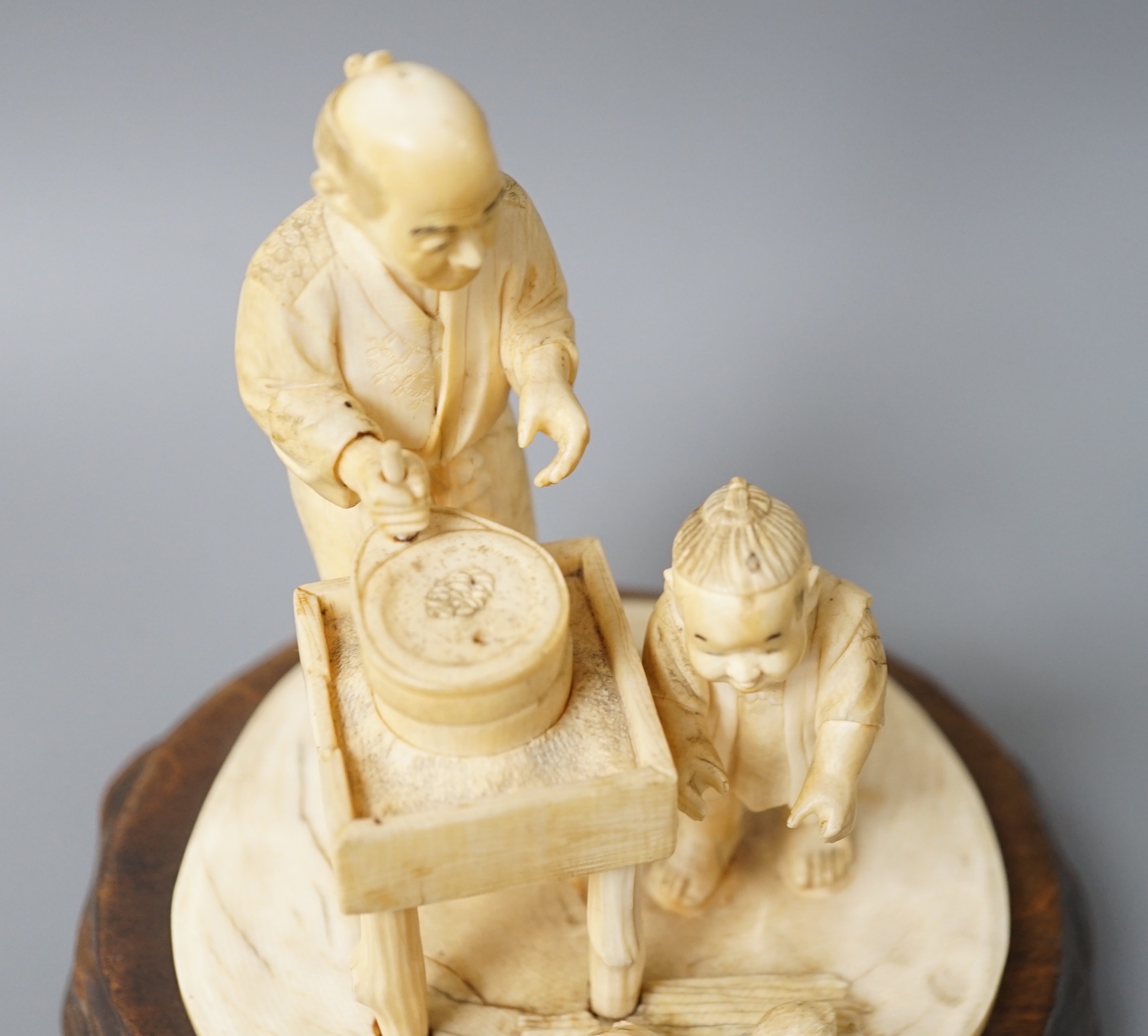 A Japanese ivory okimono of man and boy at a grindstone, Meiji period, signed, wood stand. 15cm total height